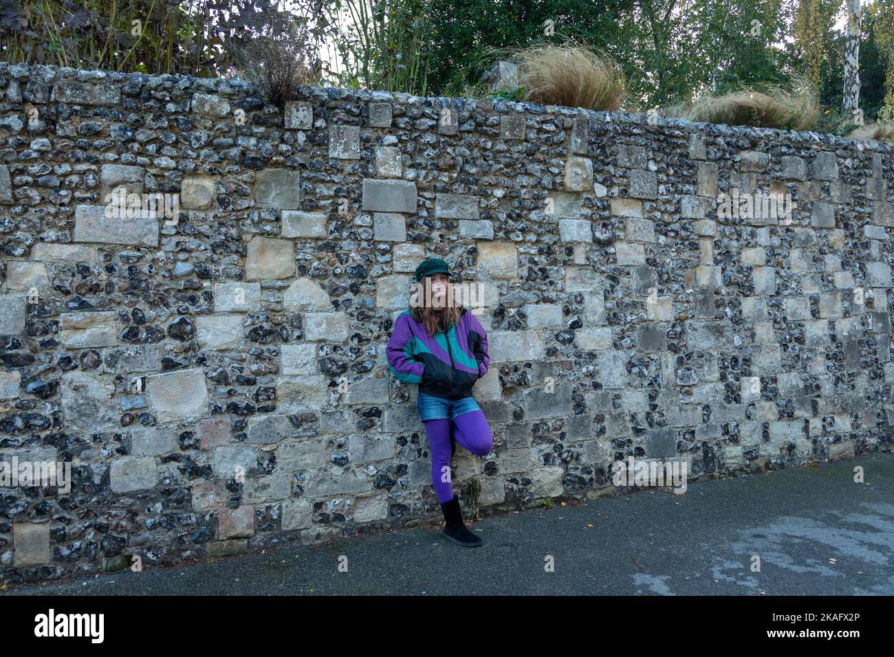 Bunt gekleideter Teenager, der sich an eine Wand lehnt, Cathedral Park, Canterbury, Kent, England, Großbritannien Stockfoto