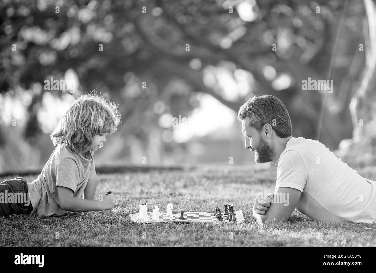 Glückliche Familie von Vater und Sohn Kind spielen Schach auf grünem Gras im Park im Freien, Schach Stockfoto