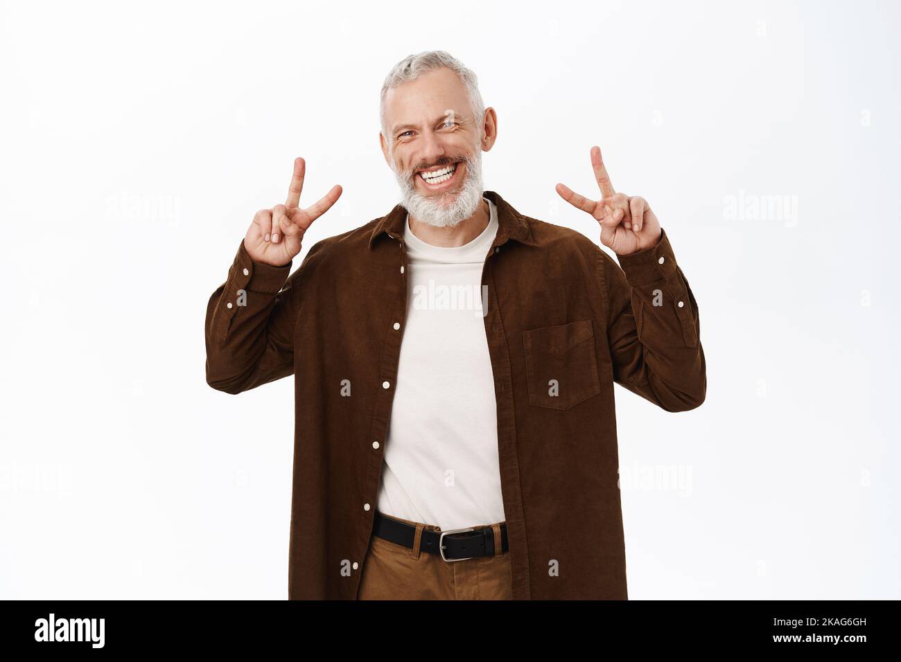 Gutaussehender älterer Mann, altes männliches Model, lächelnd, mit V-Zeichen-Geste, sorglos in legerer Kleidung vor Studiohintergrund stehend Stockfoto