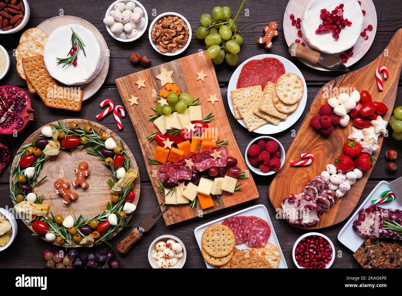 Weihnachtliche Tischszene mit Charcuterie vor dunklem Holzhintergrund. Auswahl an Käse- und Fleischgerichten. Weihnachtsbaum, Kranz und Zuckerrohr arra Stockfoto