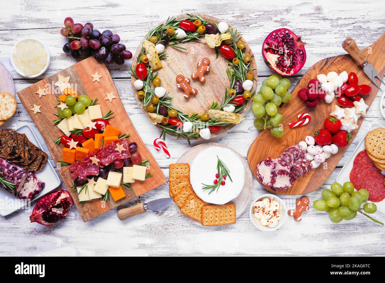 Weihnachtliche Tischszene auf weißem Holzhintergrund. Auswahl an Käse- und Fleischgerichten. Weihnachtsbaum, Kranz und Zuckerrohr arrangieren Stockfoto