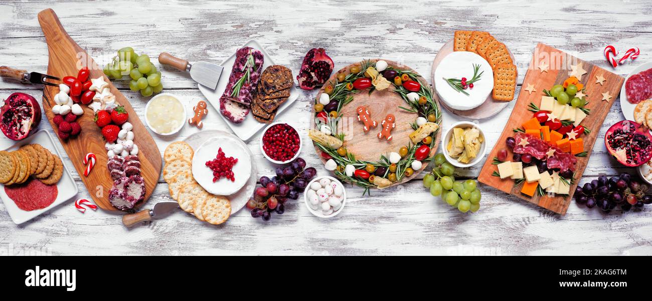 Weihnachtskarcuterie Tischszene auf einem weißen Holzbanner Hintergrund. Auswahl an Käse- und Fleischgerichten. Weihnachtsbaum, Kranz und Zuckerrohr Stockfoto