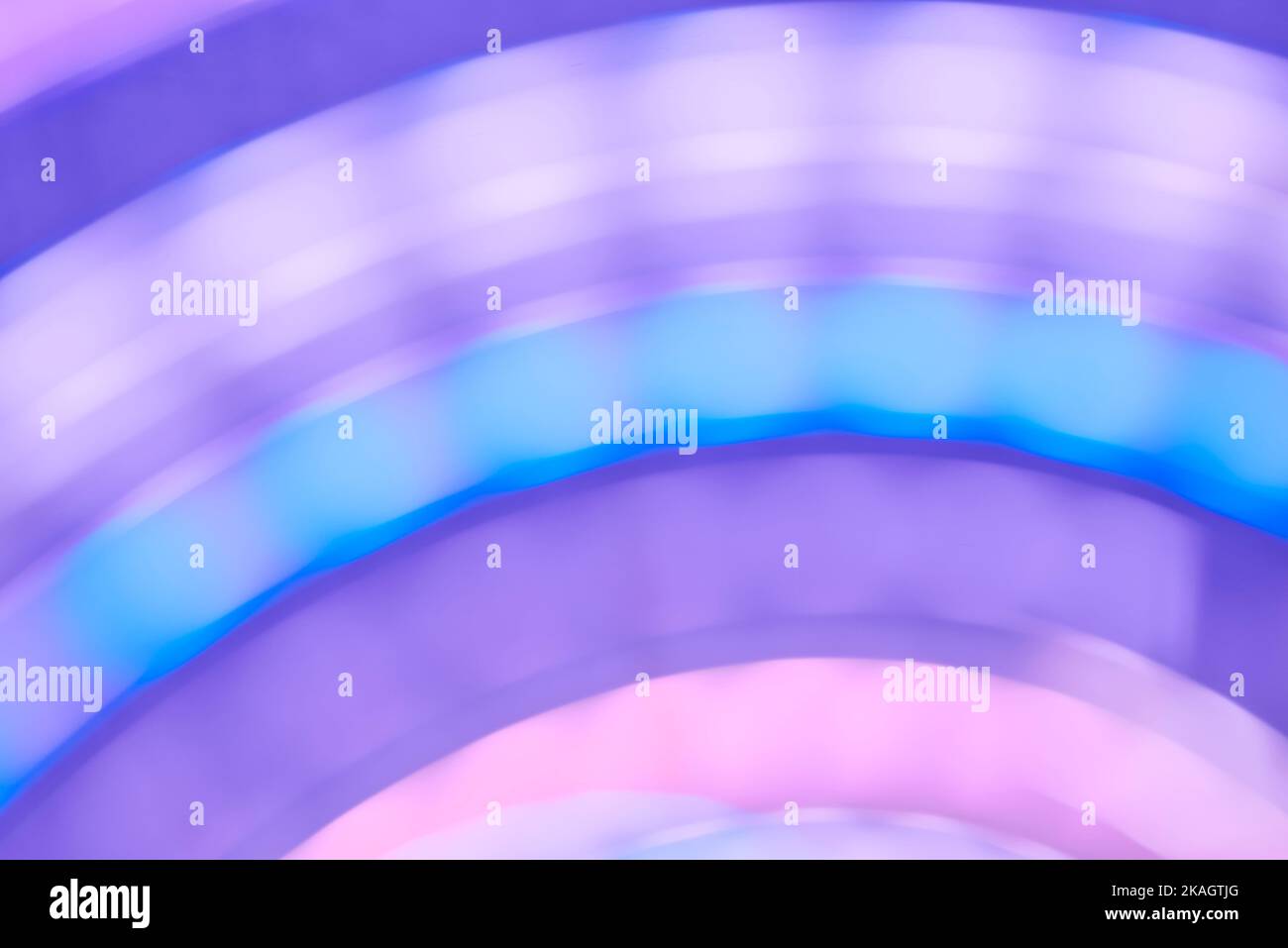 Abstrakter lila, blauer und rosafarbener Hintergrund in sanften Pastelltönen, in Bewegung geratende Farblichter schaffen ein dynamisches Design mit geschwungenen Spin-Linien. Stockfoto
