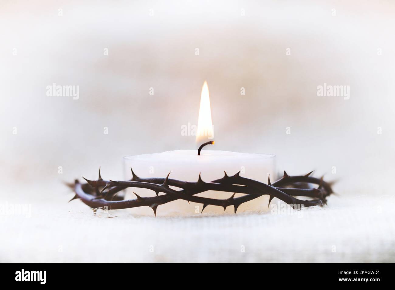 Dornenkrone, die das leidende Kreuz, den Tod und die Auferstehung Jesu Christi und den hell leuchtenden Kerzenhintergrund symbolisiert Stockfoto