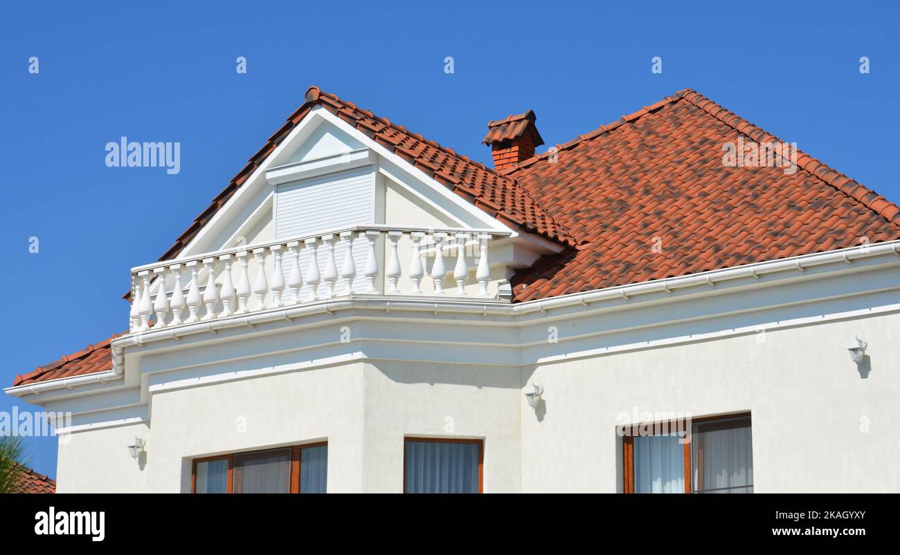 Modernes Luxushaus mit weißer Wand, Außenbeleuchtung, Balkon, Regenrinne, Keramikfliesen-Dach und Dachfenster-Rollläden. Stockfoto