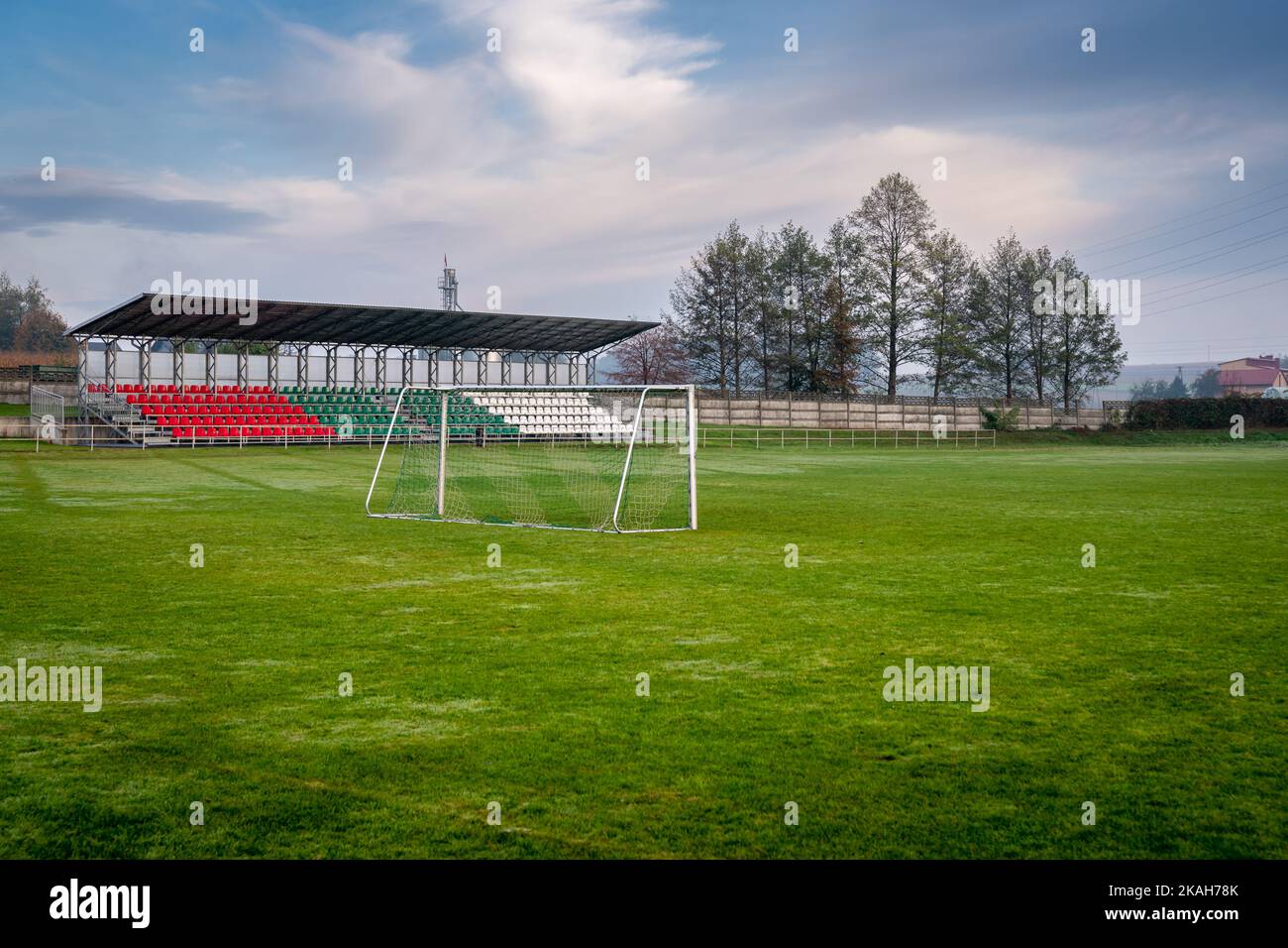 Lokales Fußballstadion mit kleinen Sport-Tribüne durch das Tor gesehen. Bäume im Hintergrund. Herbsttag auf dem Land. Stockfoto