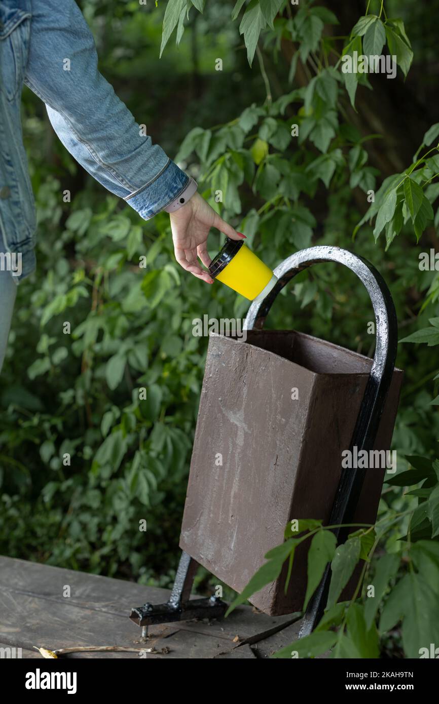 Mann wirft weg einen Papierbecher in die Urne. Hand wirft Glas. Alte Mülleimer. Kaputter Mülleimer Stockfoto