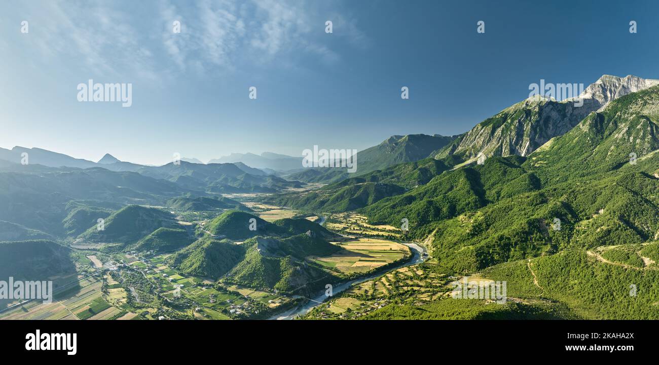 Panoramablick auf das Vjose-Tal in Albanien. Der kristallklare, türkisfarbene Fluss schlängelt sich durch Felder gegen Berge. Stockfoto