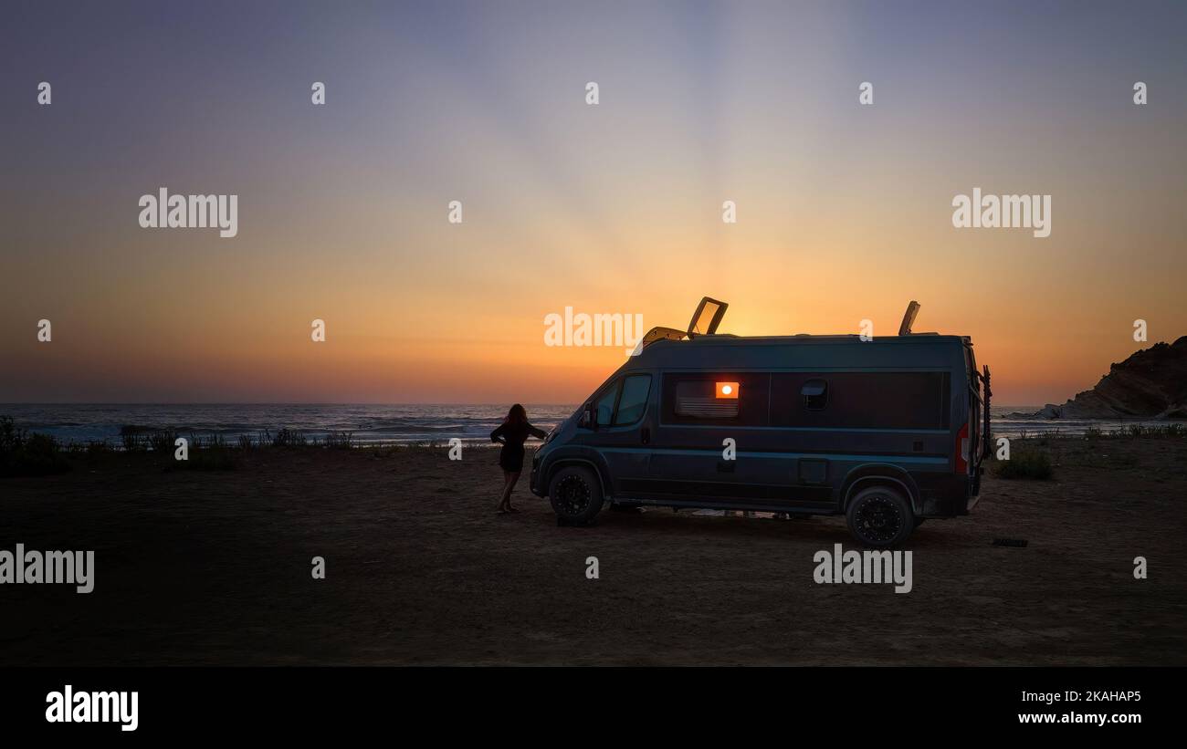 Silhouette eines Offroad-Wohnwagens gegen die untergehende Sonne, den Strand und das Meer. Abenteuer des wilden Campens, nomadisches Leben. Reisen in einem Van campe Stockfoto