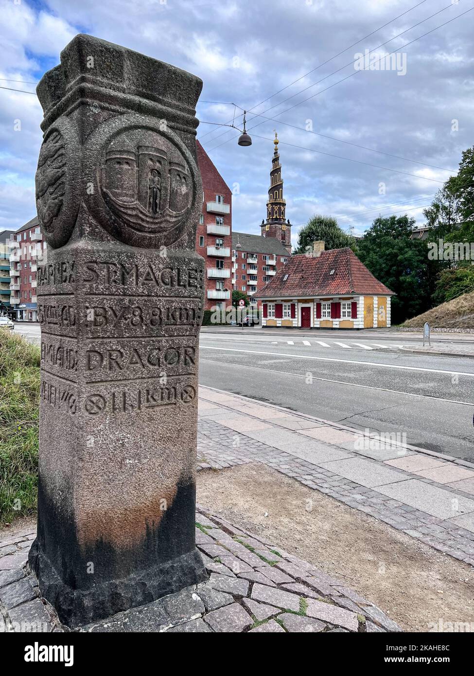 Historische Steinmeilenstein-Markierung am Straßenrand mit unserer Heiland-Kirche (vor Frelsers Kirke) in der Ferne, Christianshavn, Kopenhagen, Seeland, Dänemark Stockfoto