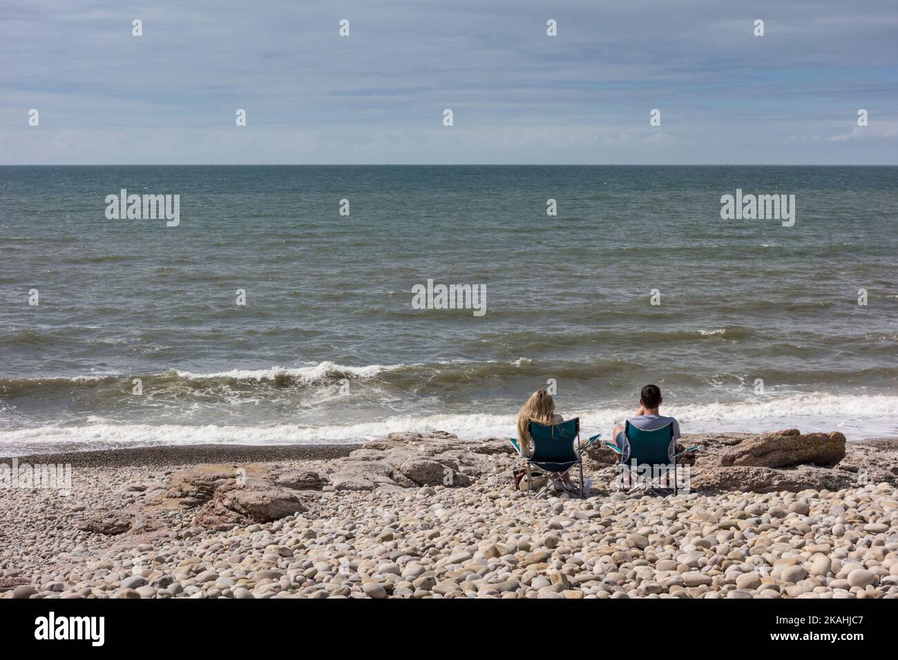 Pärchen sitzen auf Picknickstühlen und genießen den Meerblick, Ogmore by Sea, Vale of Glamorgan, Wales Stockfoto