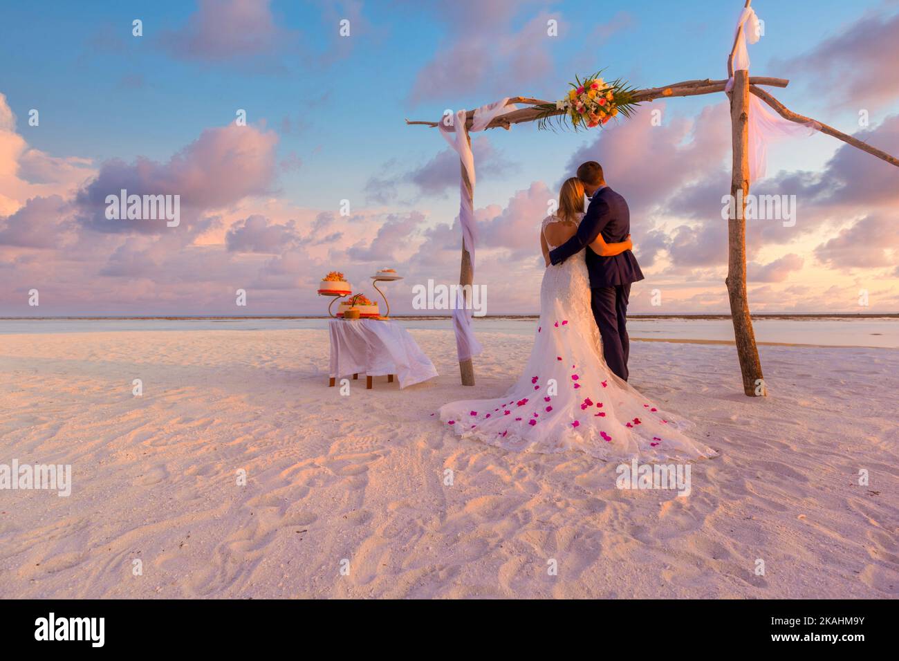 Braut und Bräutigam, Brautpaar, Flitterwochen am Strand bei Sonnenuntergang Sonne Romantik unter Hochzeitstor mit Kuchen. Liebhaber oder Neuvermählte heirateten ein junges Paar am Strand Stockfoto