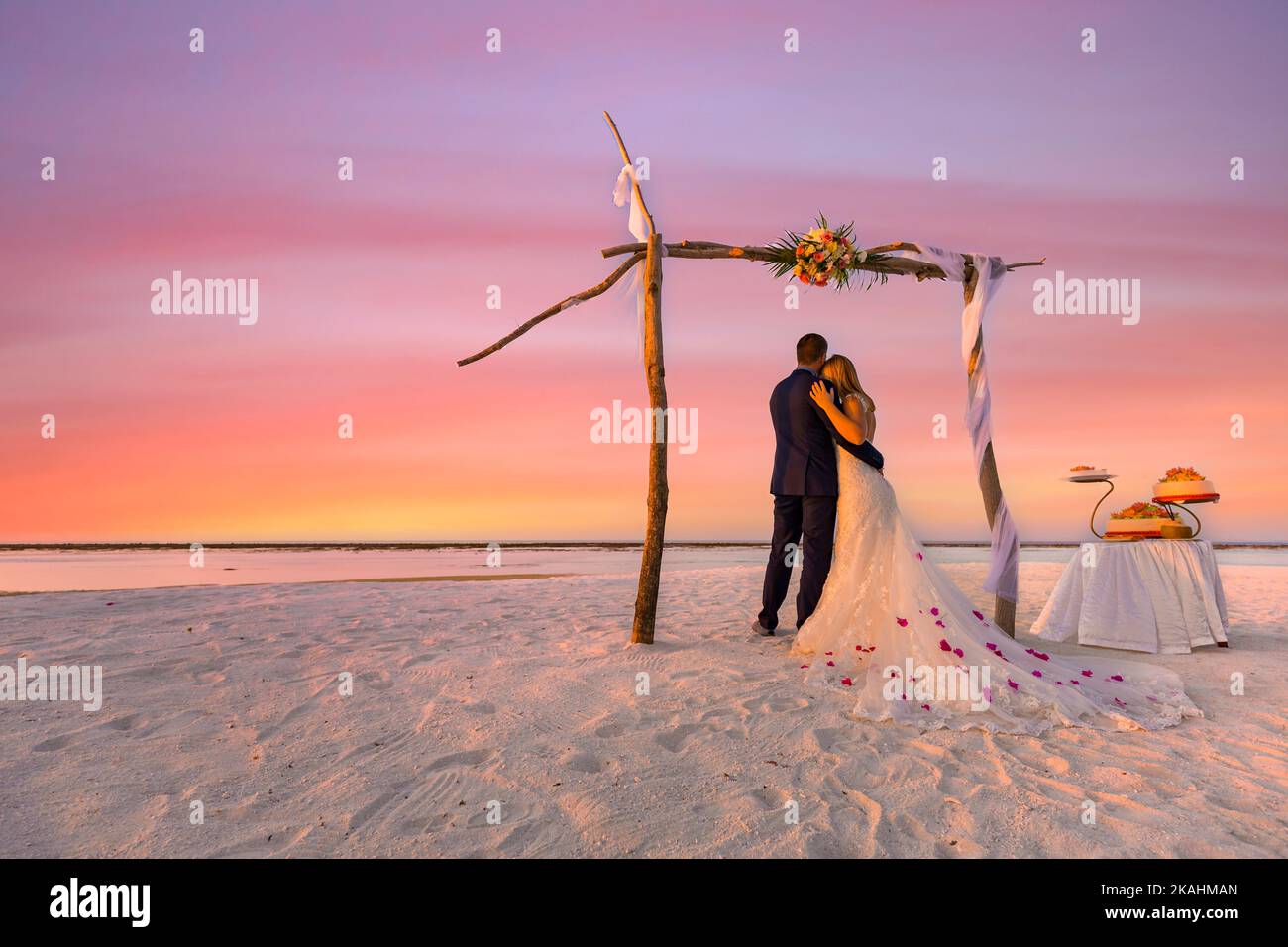 Braut und Bräutigam, Brautpaar, Flitterwochen am Strand bei Sonnenuntergang Sonne Romantik unter Hochzeitstor mit Kuchen. Liebhaber oder Neuvermählte heirateten ein junges Paar am Strand Stockfoto