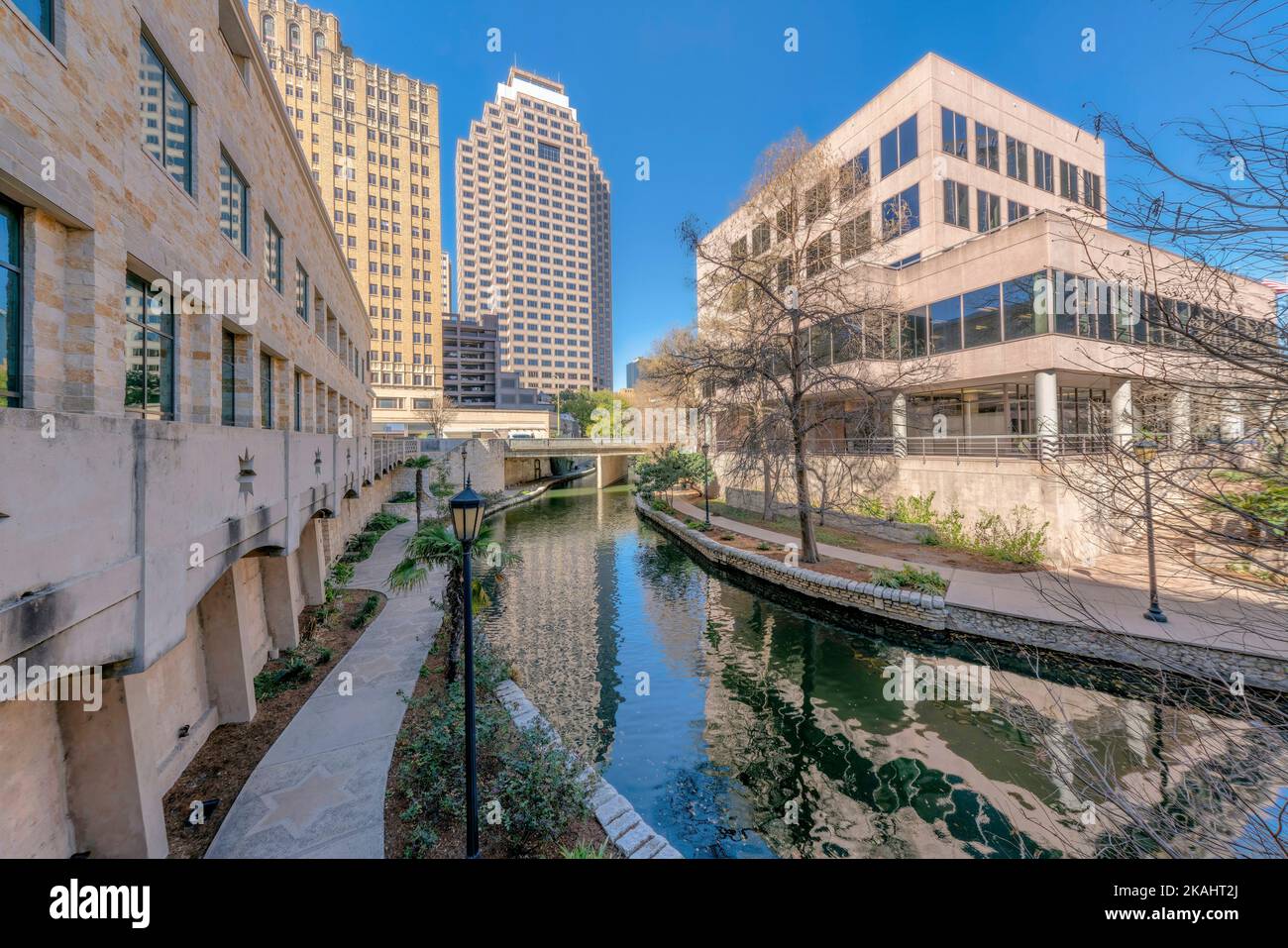 Flusswanderung in San Antonio Texas entlang hoher Gebäude mit blauem Himmel Hintergrund. Gepflasterte Pfade für Touristen, die auf dem ruhigen Wasser des laufen können Stockfoto