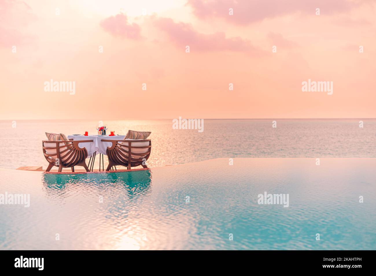 Sommer Liebe und Romantik Tisch Setup für ein romantisches Abendessen mit Luxus-Pool Reflexion Stühle unter Sonnenuntergang Himmel und Meer im Hintergrund Stockfoto