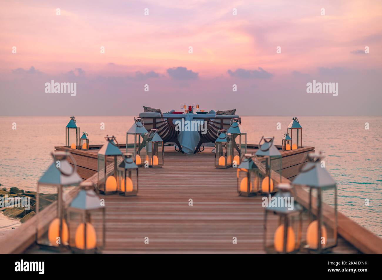 Tolles romantisches Abendessen am Strand auf der Holzterrasse mit Kerzen unter dem Sonnenuntergang. Romantik und Liebe, luxuriöses Abendessen, exotischer Tisch Stockfoto