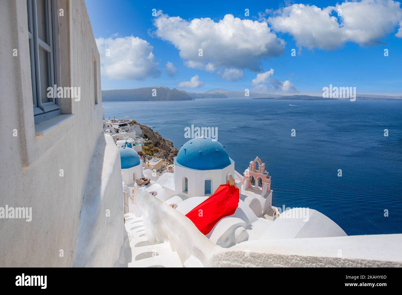 Erstaunlich elegantes Mädchen mit einem langen roten Kleid posiert über dem weißen Kirchendach in Santorini. Glücklich in Oia, Santorini, Griechenland Insel. Sorglose Mädchentour Stockfoto