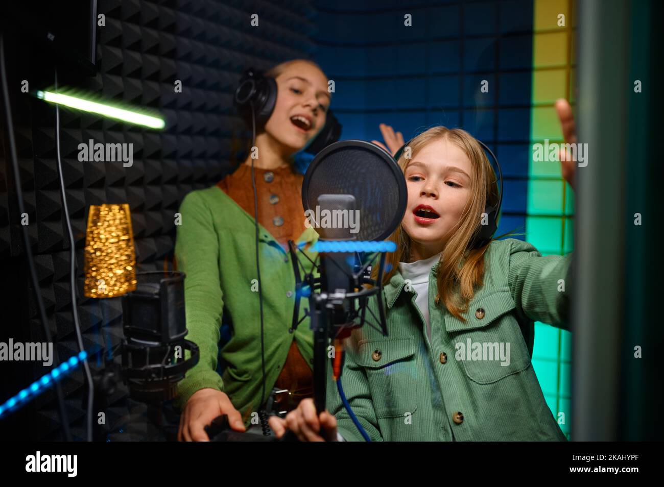Fröhliche Mädchen, die Kopfhörer tragen und im Plattenstudio singen Stockfoto