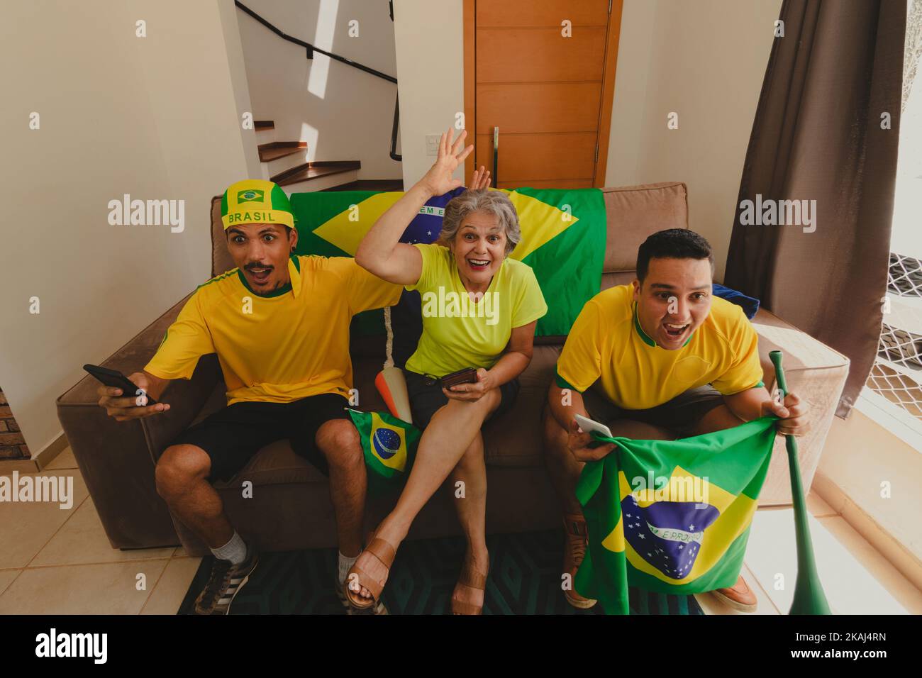 Eine Gruppe von Fußballfans feiert den Pokal im Wohnzimmer und schaut sich Fußballspiele an. Multi Ethnics Familie jubelt für Brasilien zum Champion zu werden. Stockfoto