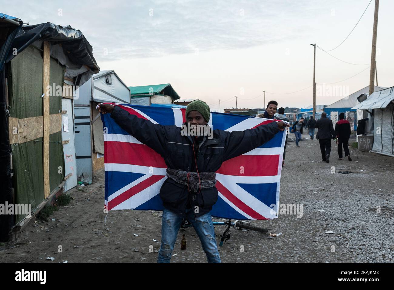 Ein Migrant posiert am 25. Oktober 2016 im Calais-Dschungel in Calais, Frankreich, mit der britischen Flagge auf der Hauptstraße. Bis zum Abend wurden etwa 4.000 Migranten aus dem Flüchtlingslager an der Küste des Ärmelkanals in mehrere Regionen Frankreichs verteilt. Die Polizei hat begonnen, die Hütten und Zelte im Lager abzureißen. (Foto von Markus Heine/NurPhoto) *** Bitte nutzen Sie die Gutschrift aus dem Kreditfeld *** Stockfoto