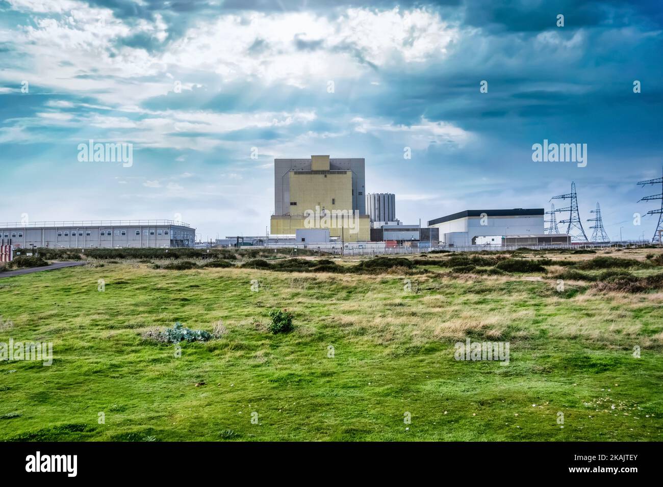 Das Kernkraftwerk Dungeness liegt in einer düsteren, leeren Landschaft, in der die Sonne durch die Wolken bricht Stockfoto
