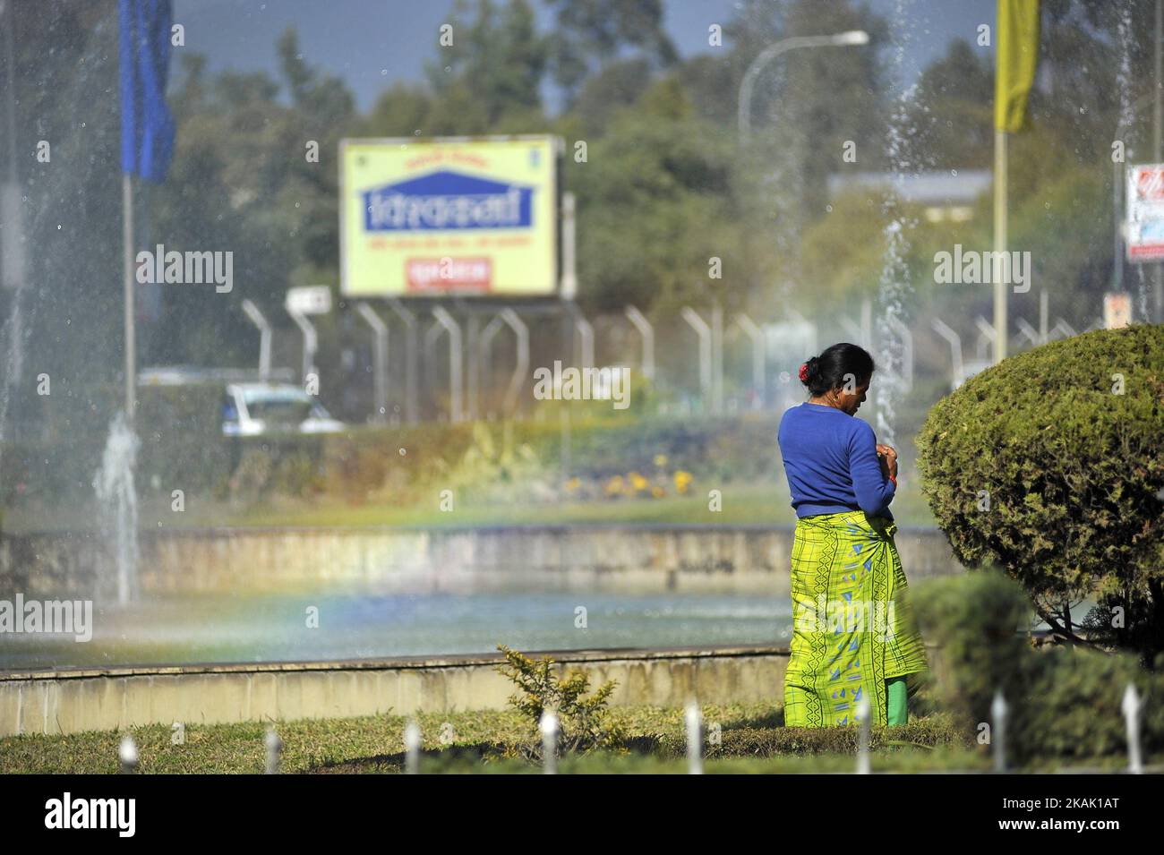 Eine Frau rast kurz aus, als sie am Freitag, den 16. Dezember 2016 im Garten des Internationalen Flughafens Tribhuwan in Kathmandu, Nepal, als Regenbogen aus Wasserbrunnen im Hintergrund arbeitete. (Foto von Narayan Maharjan/NurPhoto) *** Bitte nutzen Sie die Gutschrift aus dem Kreditfeld *** Stockfoto