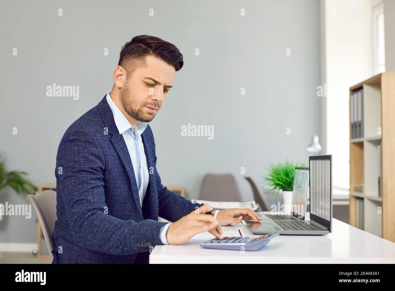 Der Finanzbuchhalter sitzt an seinem Schreibtisch und benutzt einen Rechner und einen Laptop Stockfoto
