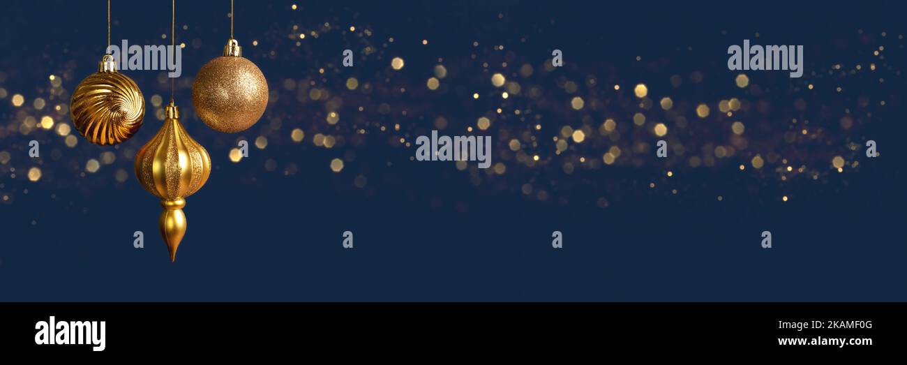 Weihnachtsbanner mit drei goldenen Kugeln Dekorationen auf blauem Hintergrund mit Bokeh-Lichtern mit Kopierraum. Weitwinkelvorsatz Stockfoto