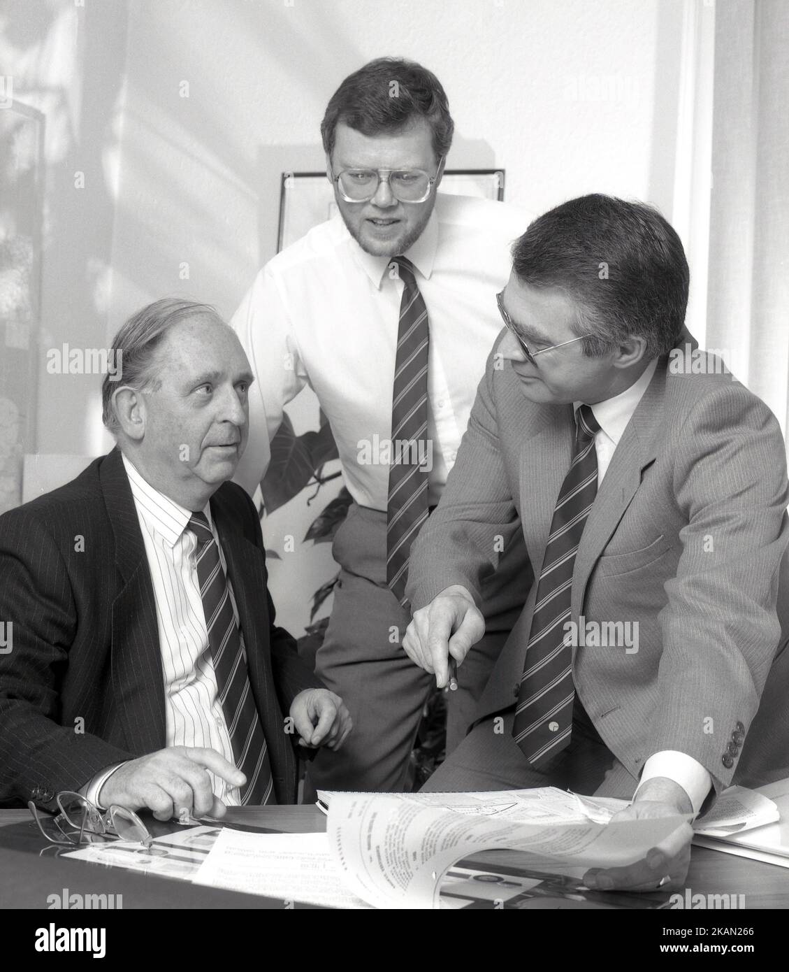 1989, historisch, in einem Büro, versammelten sich drei leitende Führungskräfte eines Unternehmens, um einen Bericht zu betrachten, England, Großbritannien. Stockfoto