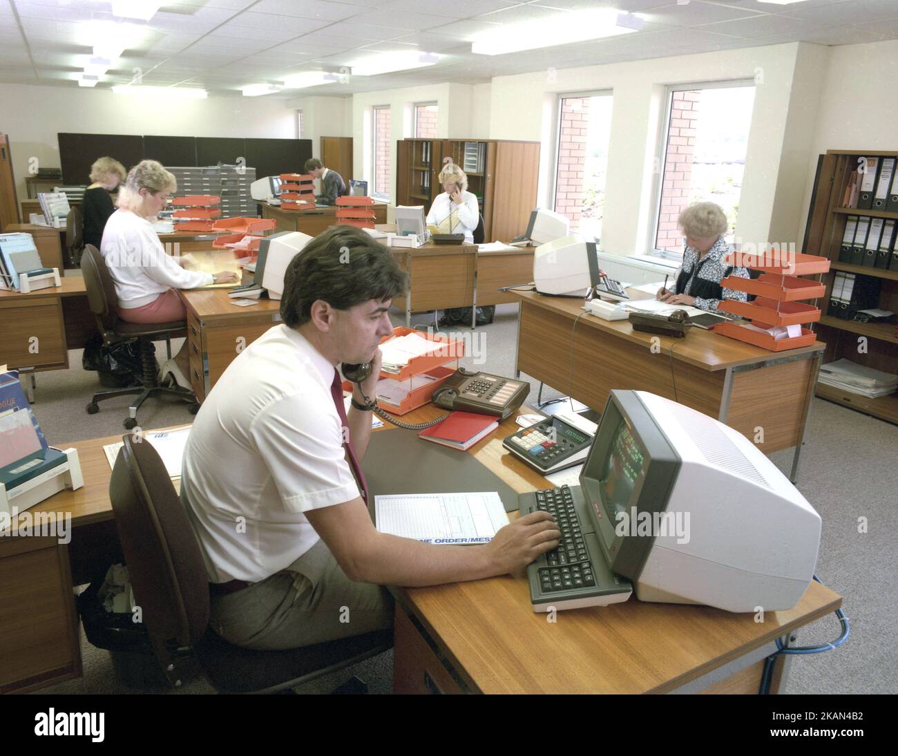 1989, historische Großraumbüros, Angestellte an Schreibtischen, einige am Telefon, England, Großbritannien mit Computerkonsolen oder PCs der damaligen Zeit. Anfang 80s, als IBM seinen PC auf den Markt brachte, begann der Markt für kleine Desktop-PCs. Stockfoto