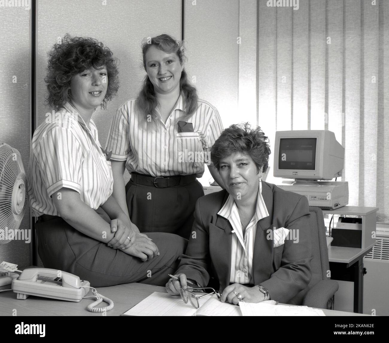 1989, historisch, in einem Büro an einem Schreibtisch, versammelten sich drei weibliche Angestellte für ein Foto, England, Großbritannien. Alle tragen Firmenuniforn, der Manager in einer Jacke. Auf dem Bild, das auf einem Schreibtisch, einem PC der damaligen Zeit, bestehend aus einem separaten VGA-Monitor und einem Computerlaufwerk, stand, machte ein Briitsh Amstrad PC2086, ein Modell, das 1988 herauskam. Stockfoto