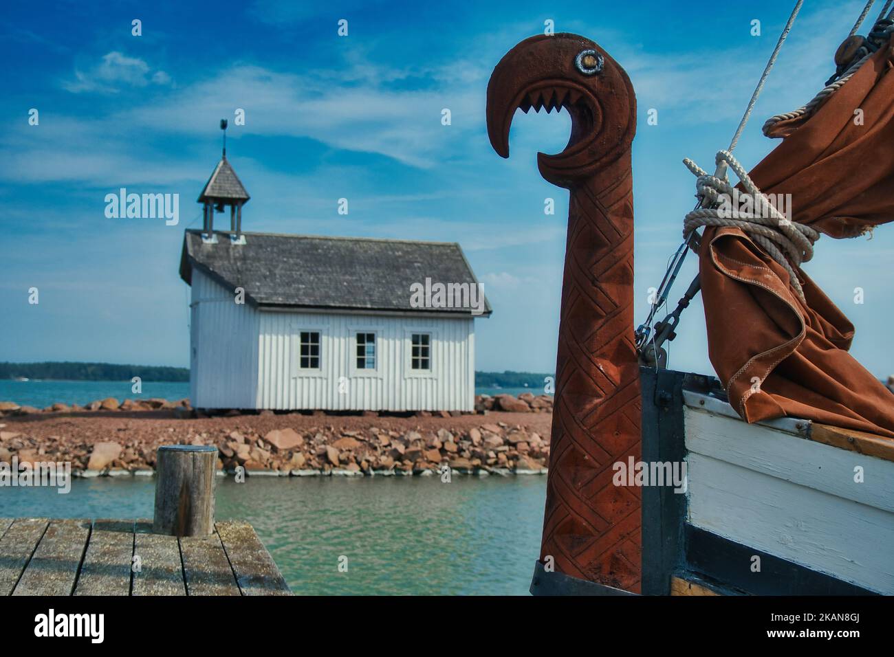 Eine kleine Holzkirche auf einer Insel mit einem wikinger-Langschiff an den Docks mit einem Drachenkopf auf dem Bug Stockfoto
