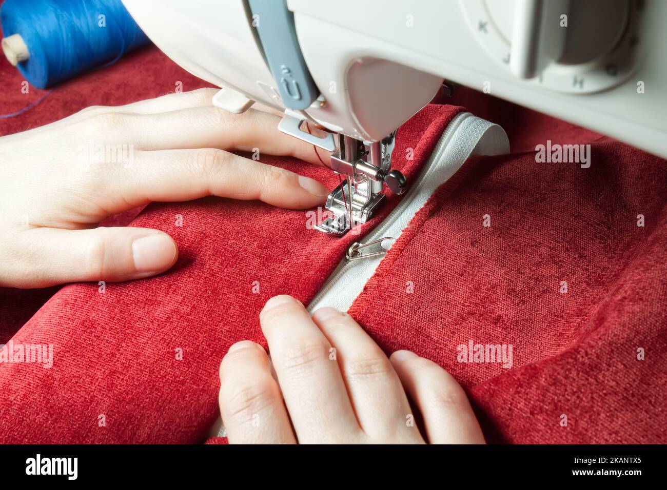 Schneiderhände nähen den Reißverschluss an roten Kleidungsstücken von einer modernen Nähmaschine mit speziellem Nähfuß. Nähprozess Stockfoto