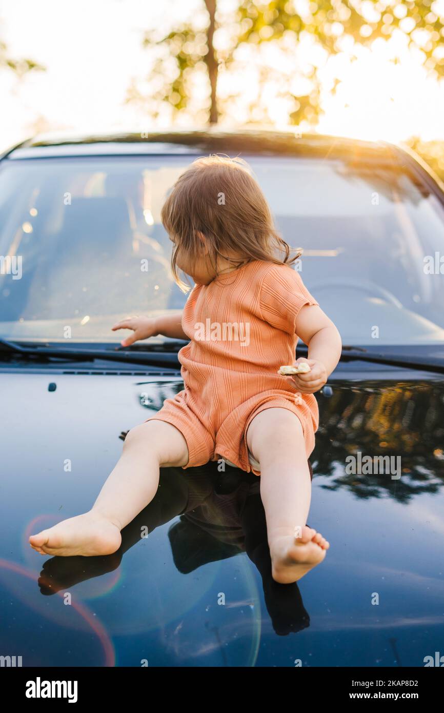 Gefährliche Position für Kinder, die draußen im Freien auf der Motorhaube des Autos stehen. Glückliche Familie, Kindheit. Sommerurlaub Spaß. Glücklich lächeln Stockfoto
