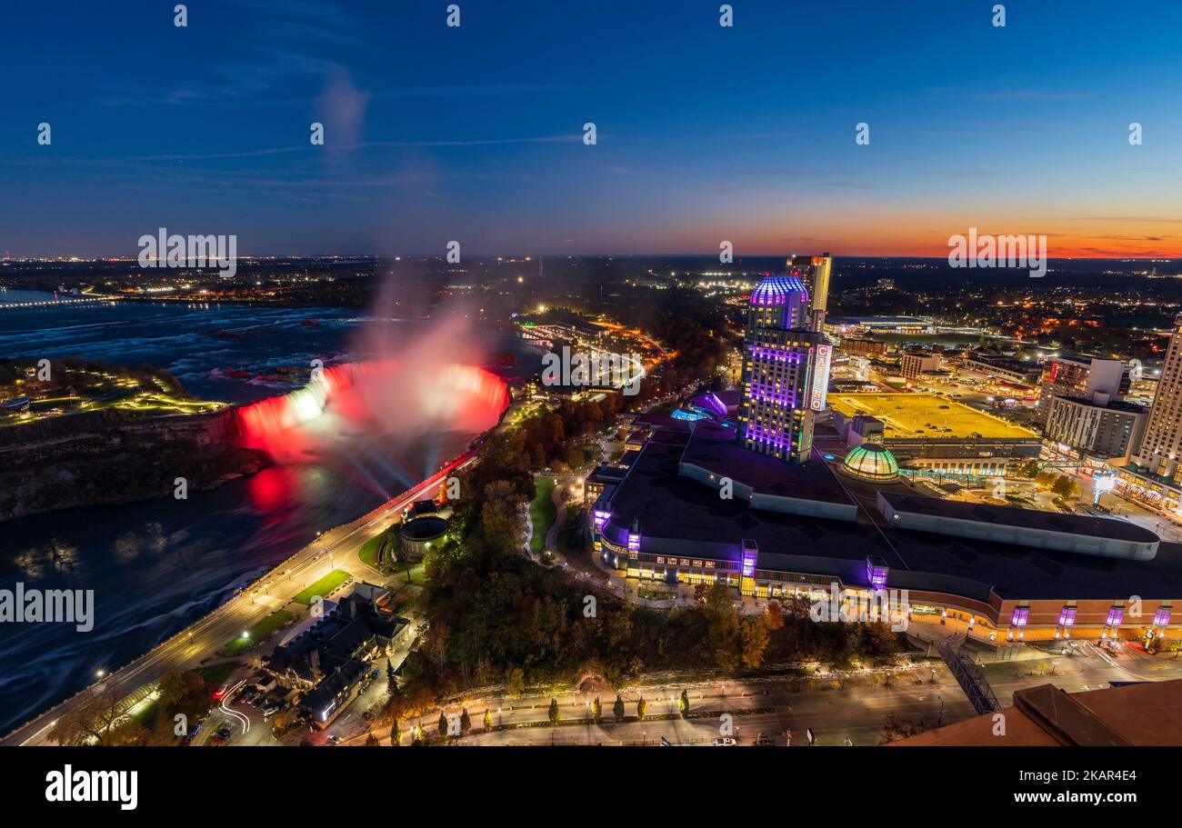 Luftaufnahme der Horseshoe Falls in der Dämmerung. Beleuchtung der Innenstadt von Niagara Falls City. Atemberaubende Landschaft bei Nacht. Stockfoto