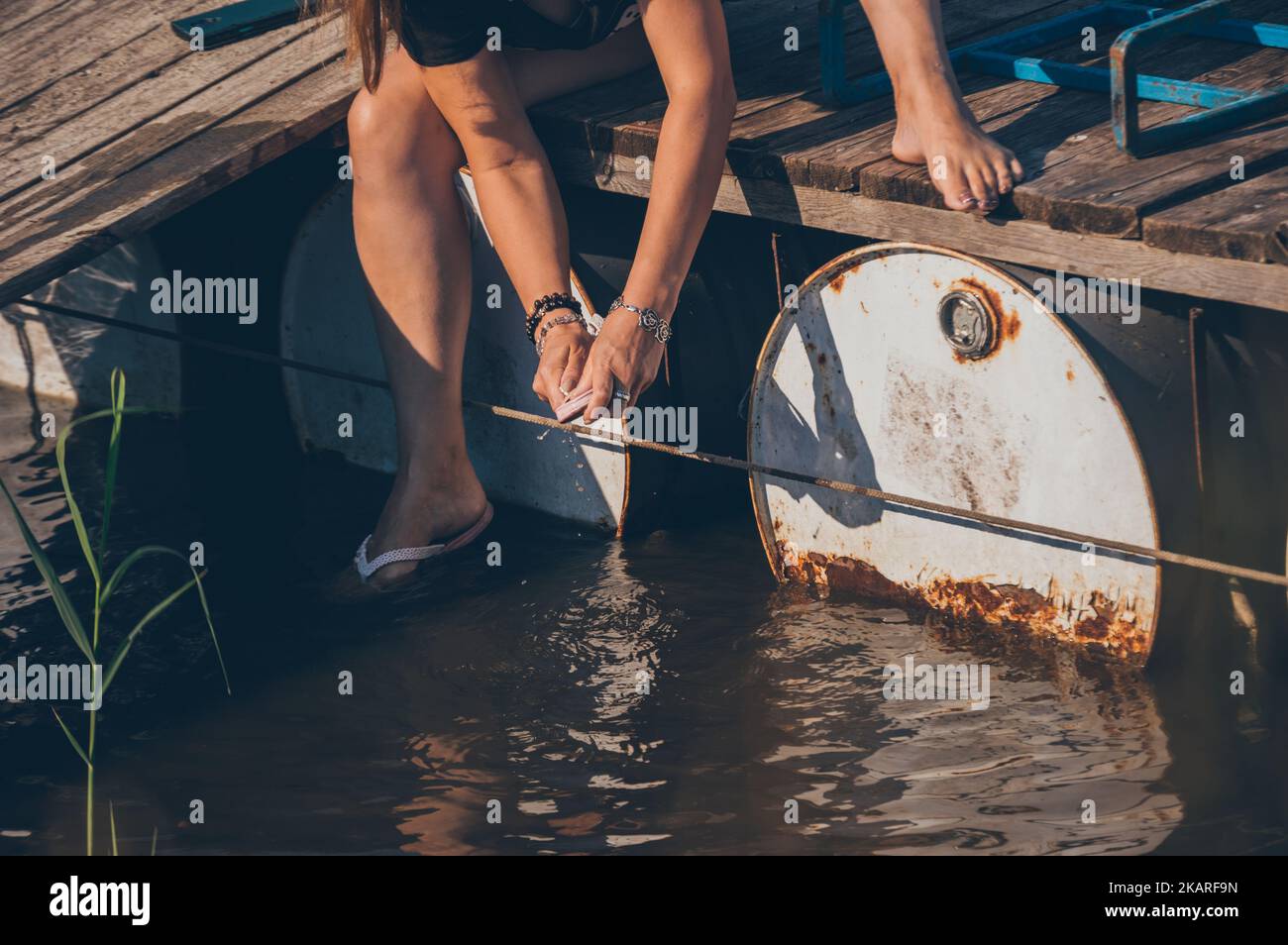 Beine einer Frau, die auf einer Holzbrücke sitzt und im Fluss den Slipper wascht Stockfoto