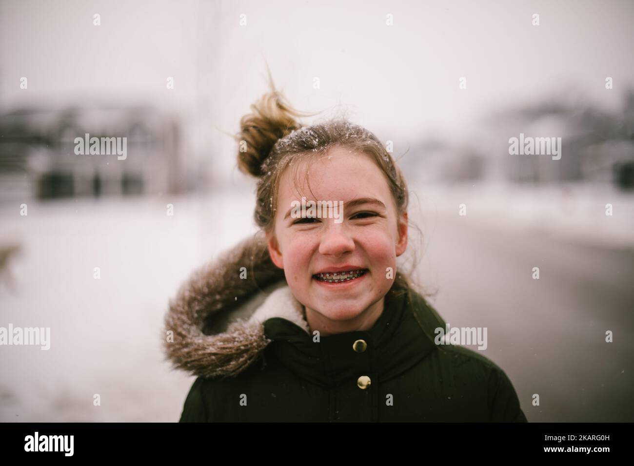 Blonde Teenager-Mädchen lächelt in verschneiten Nachbarschaft mit Schnee im Haar Stockfoto