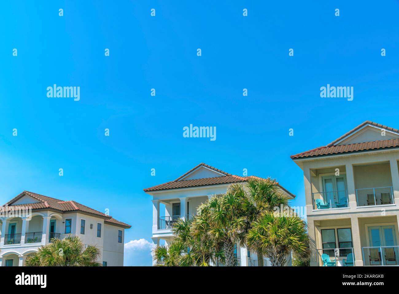 Destin, Florida- Strandhäuser mit Palmen auf der Vorderseite des Balkonen mit Sesseln. Große Strandhäuser mit Balkonen am blauen Himmel Stockfoto