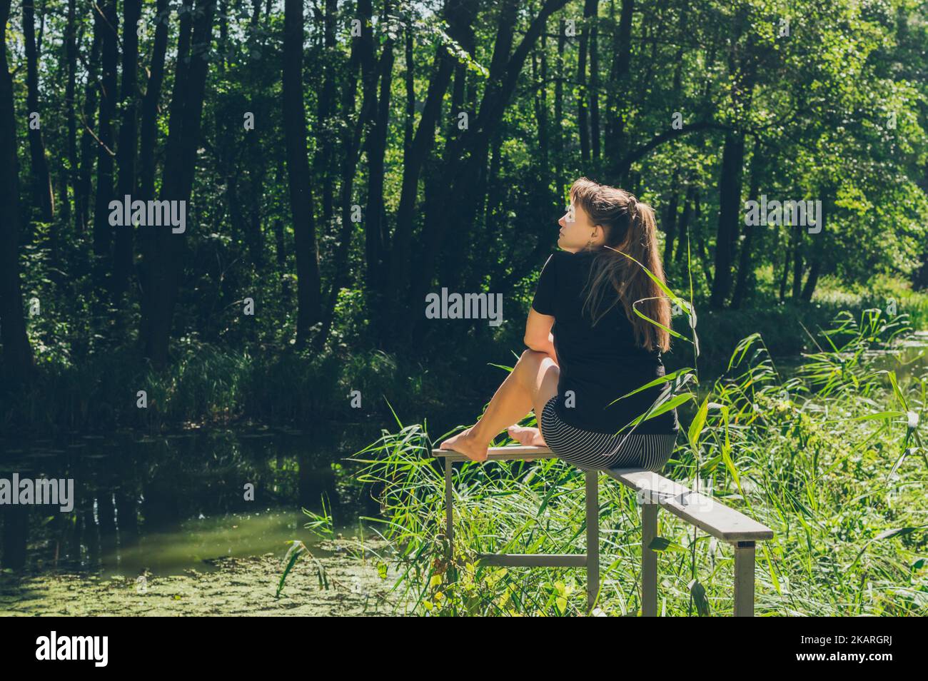 Frau sitzt und genießt Sonne und Waldlandschaft Stockfoto