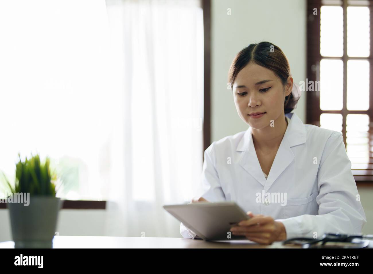Eine asiatische Ärztin verwendet einen Tablet-Computer, um die Symptome des Patienten vor der Behandlung zu analysieren Stockfoto