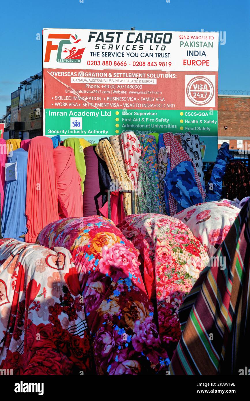 Kräftiges, farbenfrohes indisches Kleidungsmaterial, das auf einem Markt in Southall ausgestellt wird, mit einem Horten, der für ein Exportverkehrsunternehmen London England Großbritannien wirbt Stockfoto