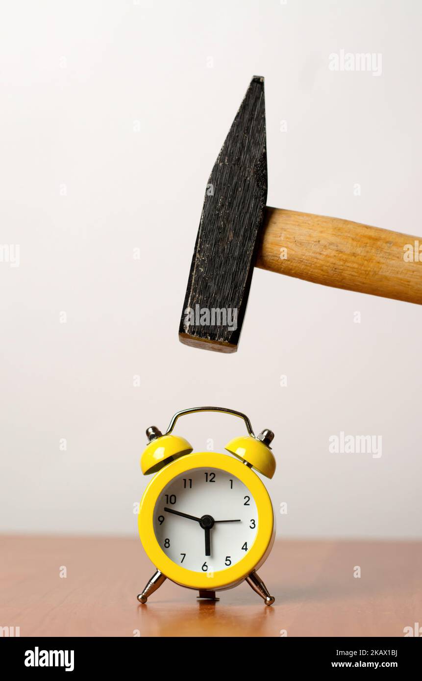 Der Hammer bricht den Wecker. Tippen Sie auf den Hammer des Weckers. Das Konzept des frühen Aufstehen zur Arbeit. Stockfoto