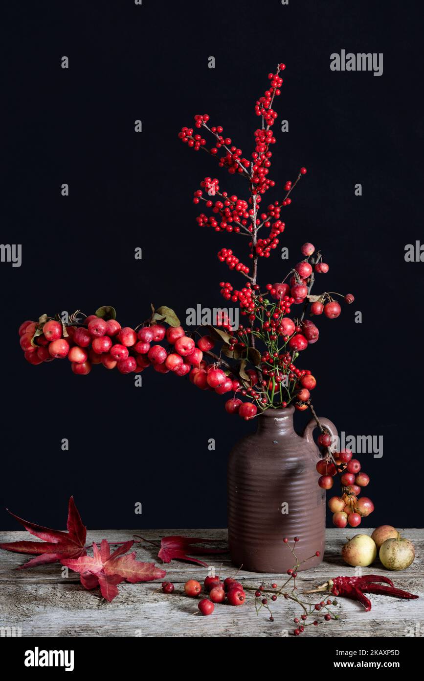 Äste von Zierapfel und Ilex in brauner Vase Stockfoto