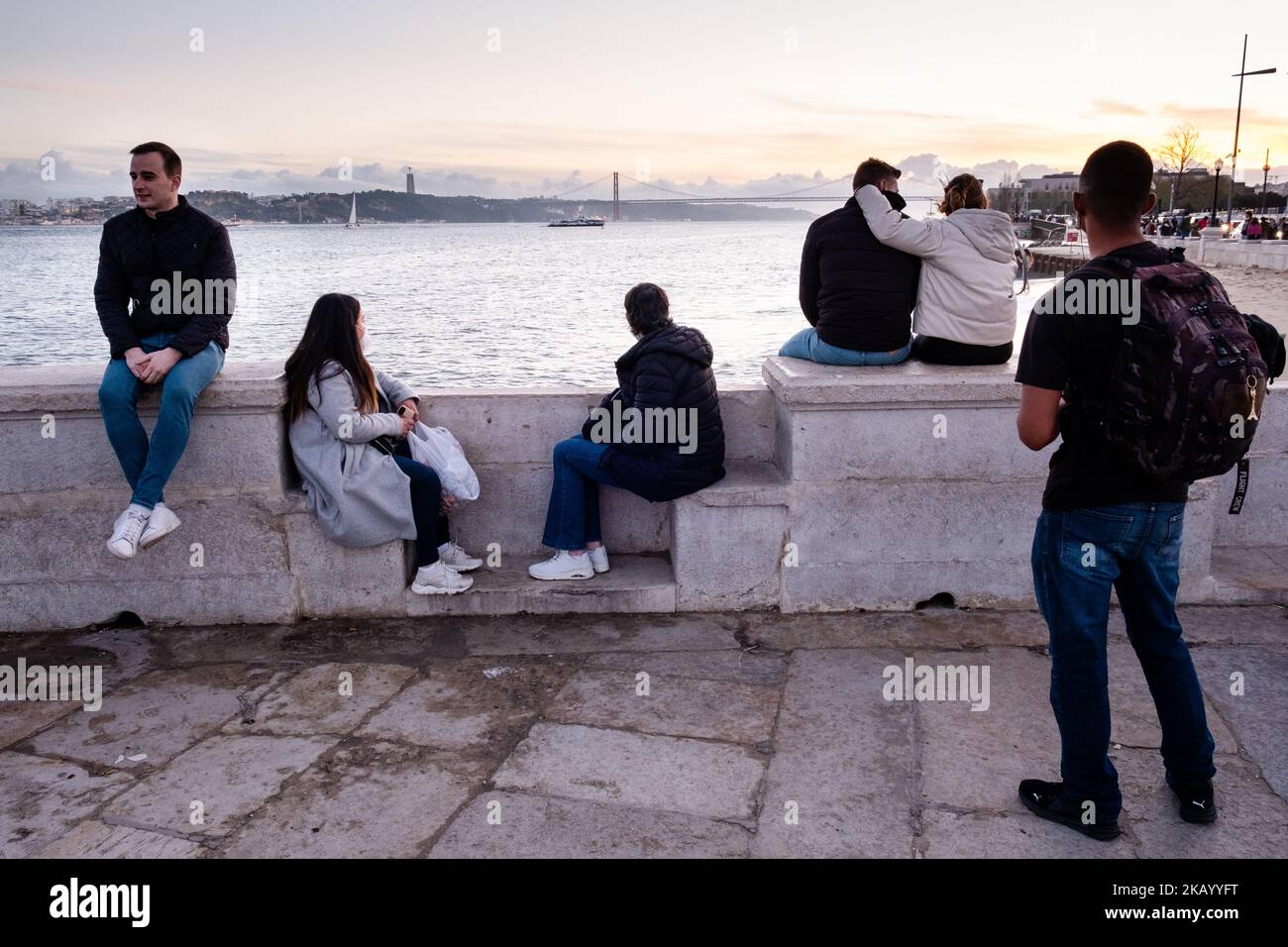 IDYLLISCHER ABEND: Touristen genießen den Blick auf die Brücke Ponte 25 de Abril und Santuário de Cristo Rei an der Promenade Tejo, Fluss Tejo (Rio Tejo), Lissabon Stockfoto