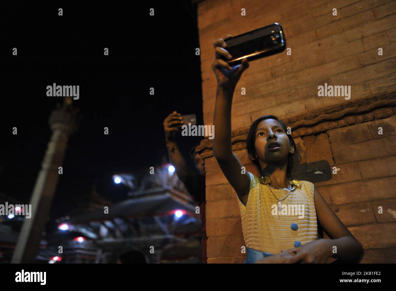 Ein kleines Mädchen fotografiert, während die jungen nepalesischen Damen und Frauen das heilige Reisbier trinken und die riesige Maske des Idols Swet Bharab während des Indra Jatra Festivals, das am Mittwoch, den 26. September 2018, auf dem Basantapur Durbar Square in Kathmandu, Nepal, gefeiert wird, aus dem Mund gießt. Indra Jatra feiert den Tag Gottes Indra, den König des Himmels. Das Indra Jatra IS Festival wird auf dem Basantapur Durbar Square, Kathmandu, Nepal, gefeiert. Indra Jatra ist eines der wichtigsten Feste Nepals, das das Ende des Monsuns feiert. Das größte Festival, bei dem Kumari in der Öffentlichkeit aufkommt, ist in Indra Jatra. Im Folgenden Stockfoto