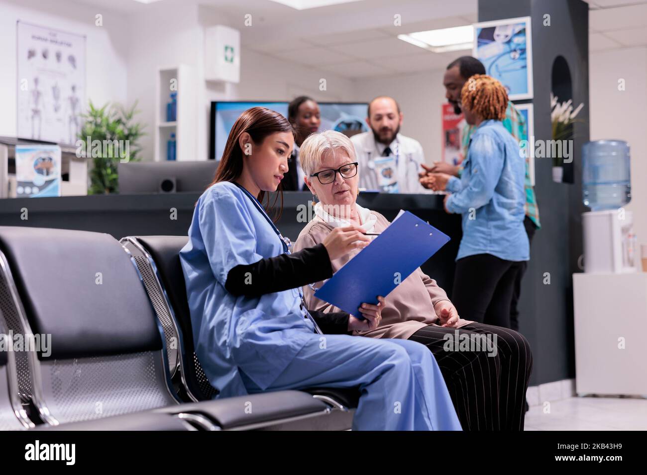 Asiatischer Gerontologiearzt, der für den Bereich der Gerontologie zuständig ist und personenbezogene Daten von älteren Patienten anfordert. Medizinisches Klinikpersonal an der Rezeption, das afroamerikanische kranke junge Paare besucht. Stockfoto