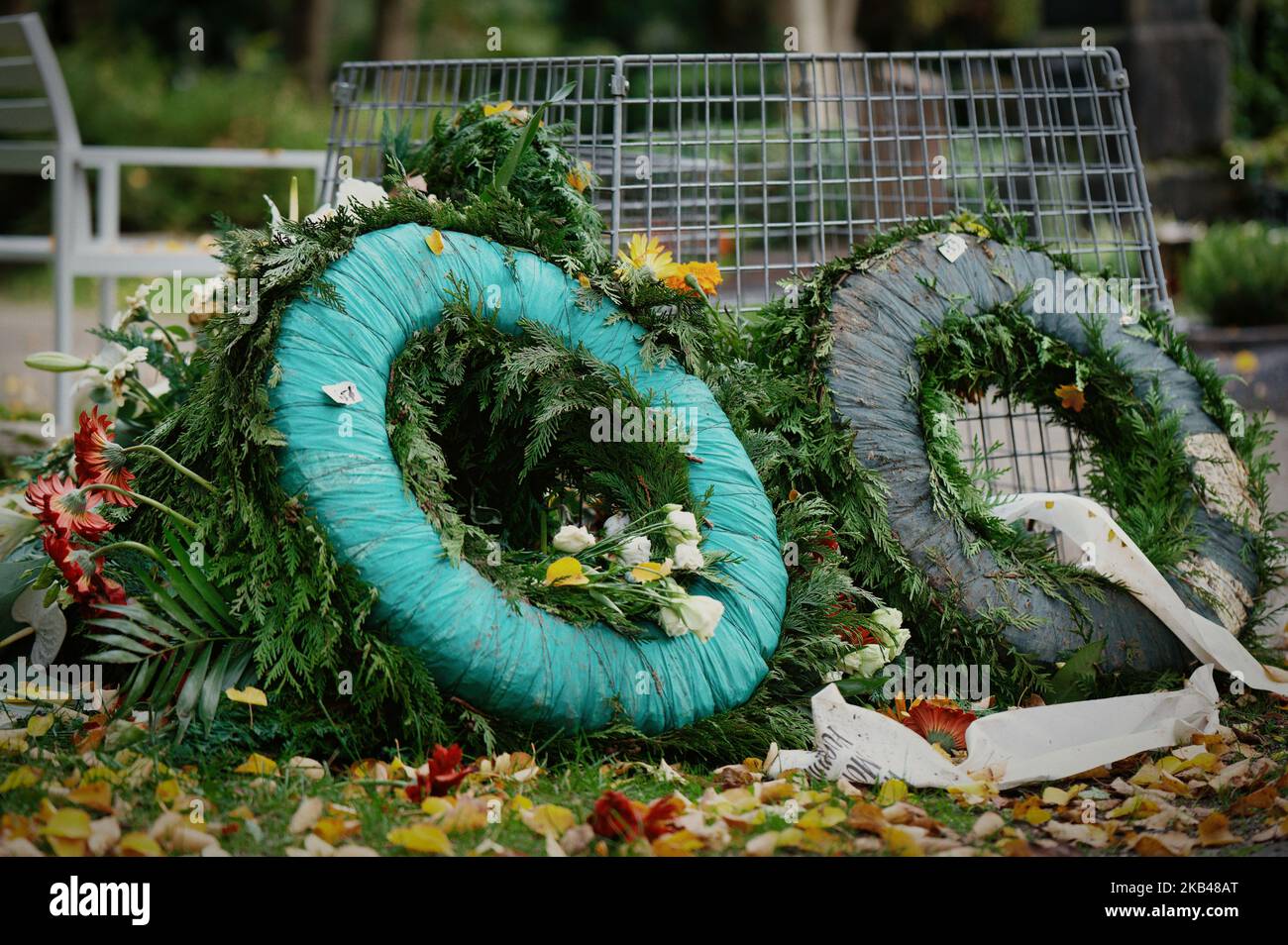 Alte Trauerkränze neben einem Abfallkorb auf einem Friedhof Stockfoto