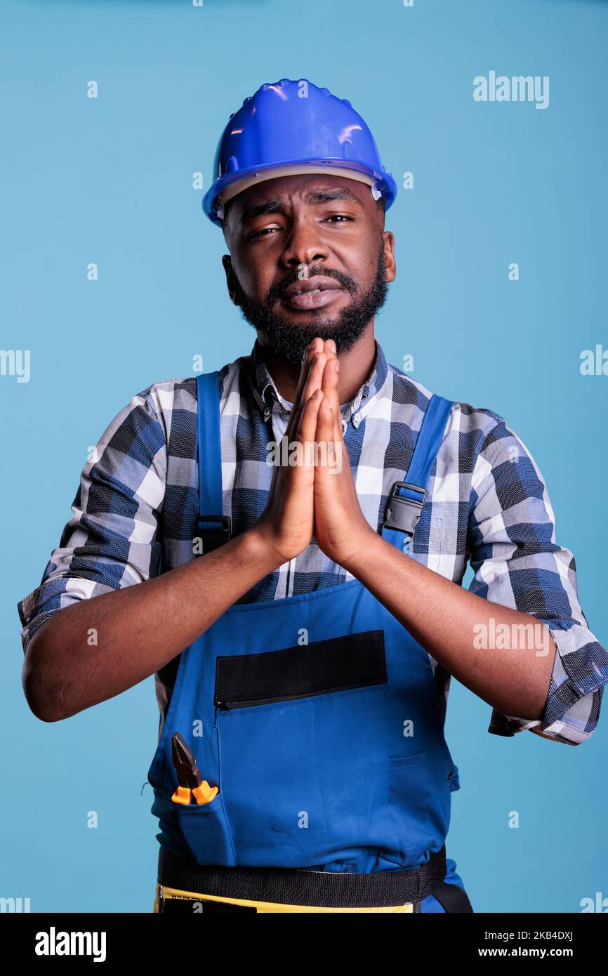 afroamerikanischer Baumeister tut Gebet Hände auf Kamera, bettelt und bittet um Glück und Glück. Bauarbeiter warten auf Wunsch oder Anfrage und flehen um Wunsch, Studio-Aufnahme. Stockfoto