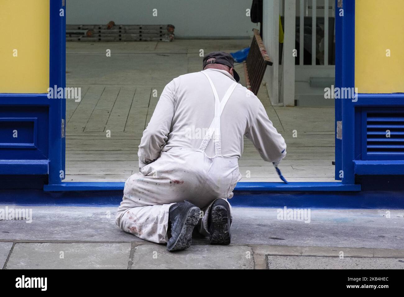 Rückansicht eines Mannes, der den Eingang des Türrahmens zum Gebäude lackiert Stockfoto