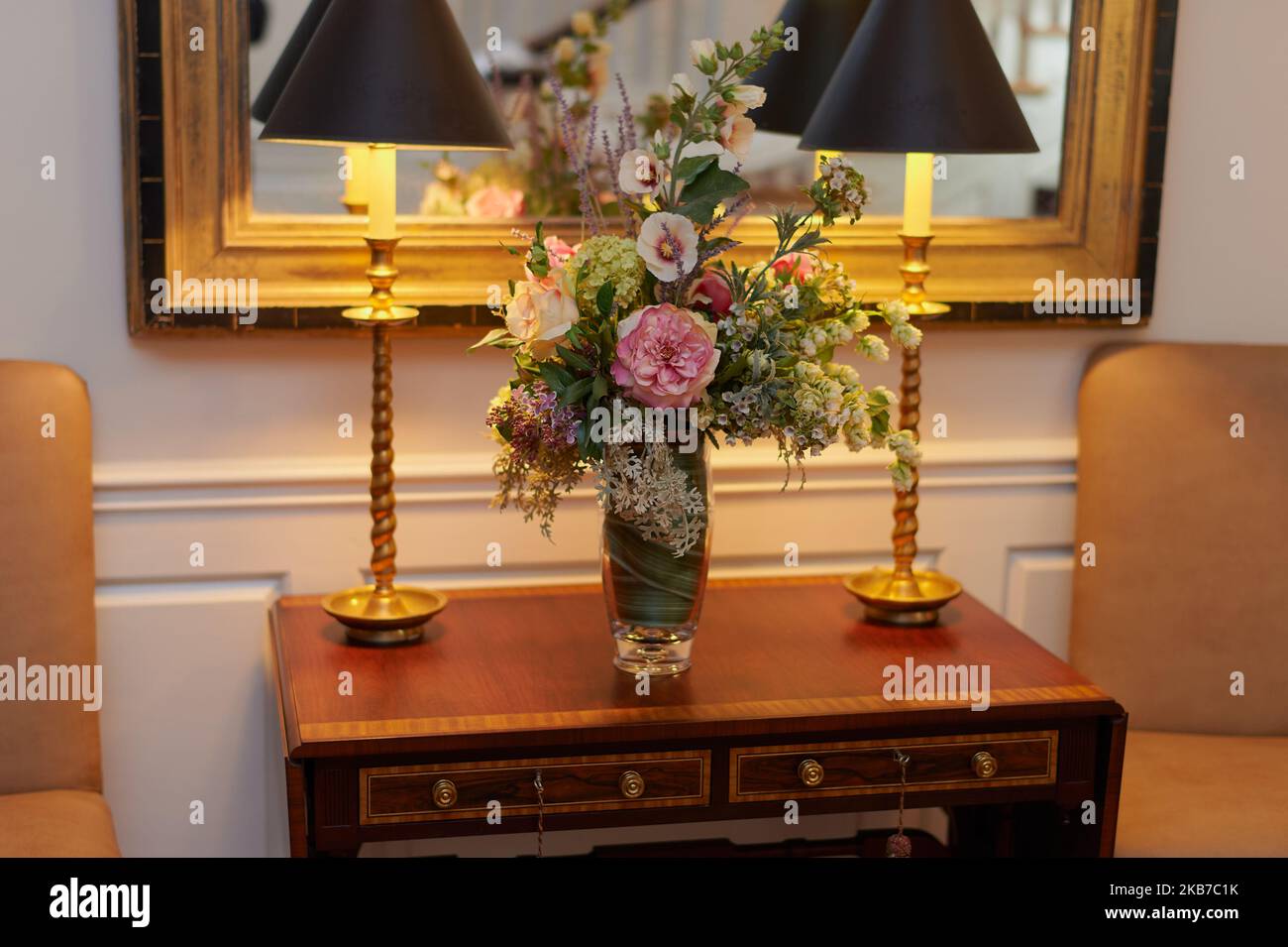 Blumenstrauß auf einem Tisch mit zwei schattigen Lampen vor teilweiser Spiegelsicht Stockfoto